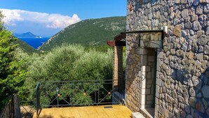 A stone building with a metal staircase leading to a balcony overlooking a mountainous landscape and a body of water.
