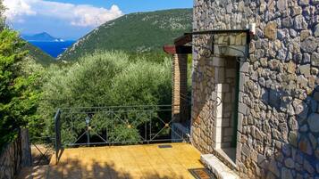 Un edificio in pietra con una scala in metallo che conduce a un balcone affacciato su un paesaggio montuoso e un corpo d'acqua.
