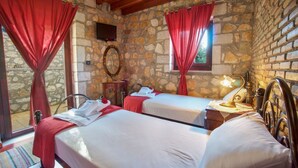 Una habitación con dos camas, paredes de piedra, televisión y ventana con cortinas rojas.