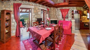 Un comedor acogedor con pared de piedra, vigas de madera, chimenea y vistas al exterior.