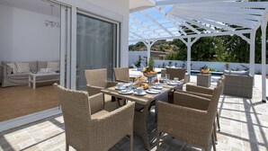 En uteplats med möbler i rotting, ett matbord med plats för fyra personer och en vit pergola.