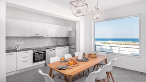 Una cocina moderna con armarios blancos, una mesa de comedor de madera y un amplio ventanal con vista al mar.