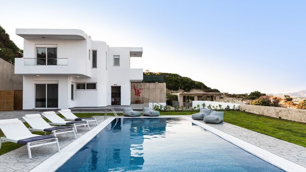 Una casa moderna de dos pisos con piscina, sillas de descanso y vista al paisaje.