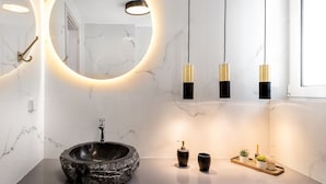 Un baño moderno con un espejo redondo grande, un lavabo de piedra y luces colgantes.
