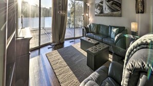 Un salón espacioso con un ventanal grande, un ventilador de techo, un sofá, una mesa de centro y un cuadro de un barco en la pared.