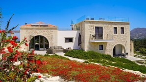 A modern two-story house with stone walls, a balcony, and a garden with red flowers. - Villa Armenoi - Three Bedroom Villa, Sleeps 8 (Apokoronos)