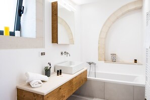 Ein modernes Badezimmer mit einem Holz-Waschtisch, einem weißen Waschbecken und einer freistehenden Badewanne.