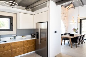 Een moderne keuken met een roestvrijstalen koelkast, houten keukenkastjes, en een eethoek met een houten tafel en stoelen.