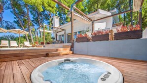 Een hottub in een houten terrasgedeelte met buitenmeubilair en een overdekte patio.