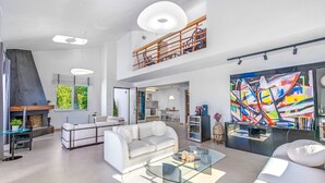 Een ruime zithoek met een moderne witte bank, een glazen salontafel en een levendig abstract schilderij.