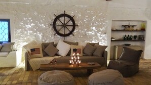 Un salon chaleureux avec un canapé, deux fauteuils en forme de poire, une table basse avec des bougies et un gouvernail de bateau fixé au mur.