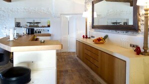 Une cuisine avec un plan de travail en bois, un évier et un miroir. Une porte donne accès à une autre pièce.