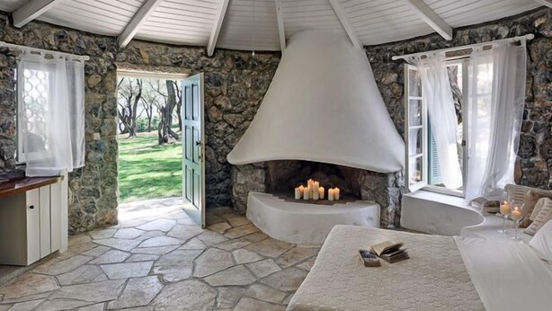A cozy room with a stone floor, a fireplace, a bed, and a view of the outdoors. - Chapel View - One Bedroom Villa, Sleeps 2 (Ionian Islands)