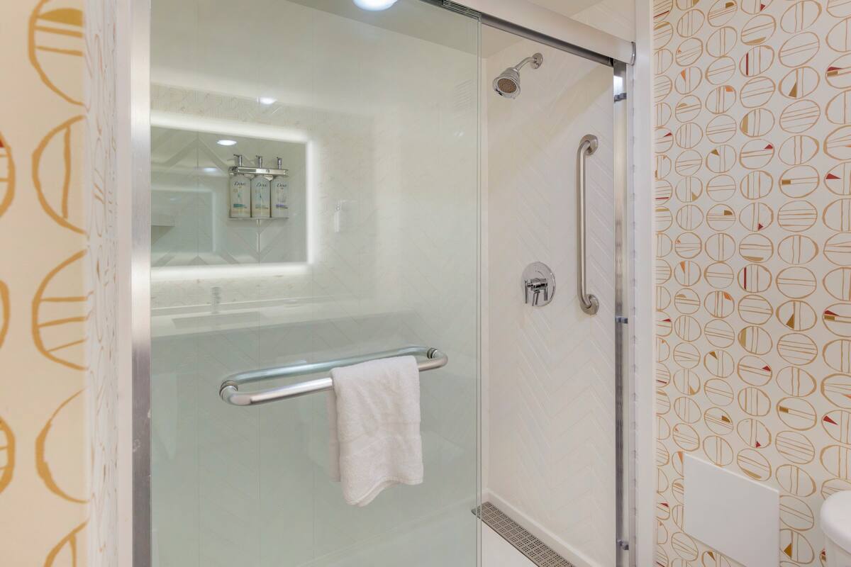 A glass-enclosed shower with a handrail and a towel rack.
