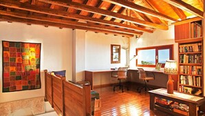 A cozy room with a wooden ceiling, a desk with two chairs, a bookshelf, and a colorful quilt on the wall.