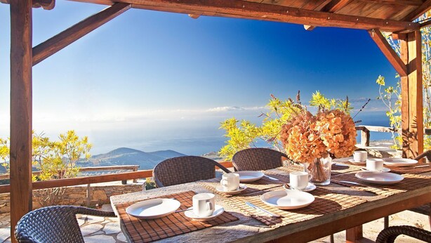 An outdoor dining area with a table set for four, overlooking a mountainous landscape.