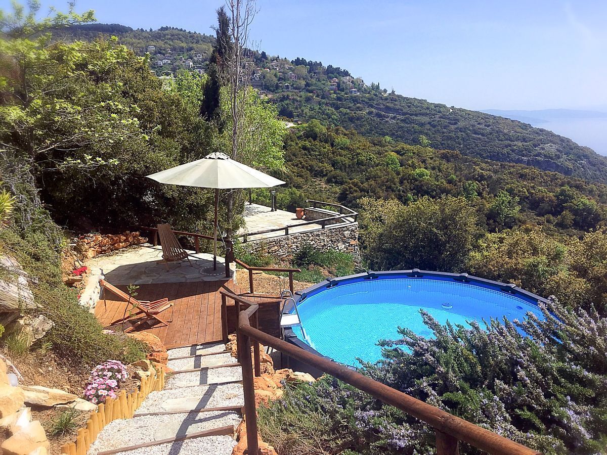A swimming pool with a wooden deck and a patio area, surrounded by lush greenery and hills in the background.