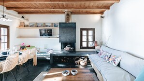 A cozy living room with a fireplace, wooden ceiling, and a sofa with colorful cushions. - Villa Artemida - Three Bedroom Villa, Sleeps 8 (Agios Georgios Nilias)
