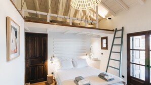 A bedroom with a loft-style ceiling, a bed with white linens, a wooden floor, a ladder, and a window with a view. - Villa Artemida - Three Bedroom Villa, Sleeps 8 (Agios Georgios Nilias)