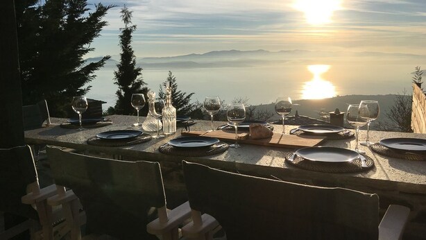 An outdoor dining area with tables set for a meal, overlooking a scenic view of the ocean and mountains. - Villa Artemida - Three Bedroom Villa, Sleeps 8 (Agios Georgios Nilias)