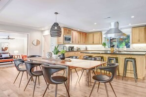 Eine moderne Küche mit Holzschränken, einer Edelstahl-Dunstabzugshaube und einem Essbereich mit Holztisch und schwarzen Stühlen.