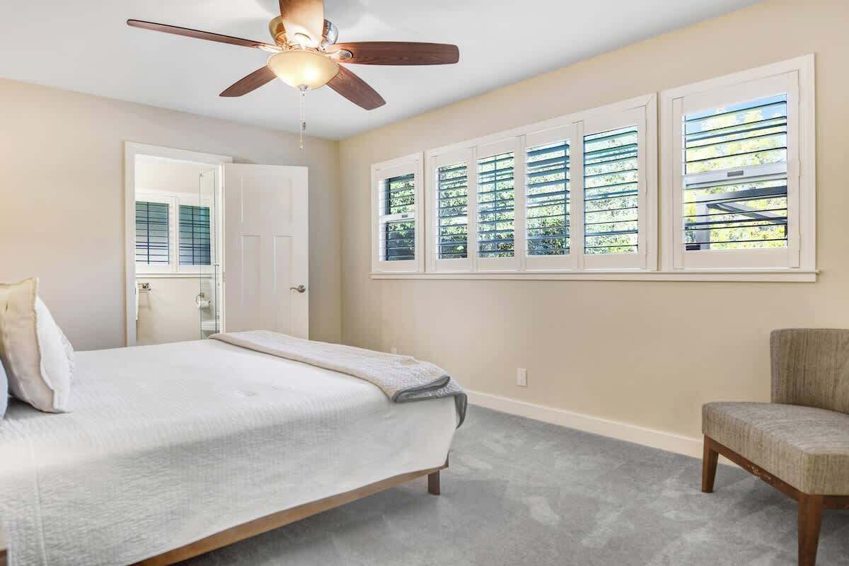 A bedroom with a bed, a chair, a ceiling fan, and a window with blinds.