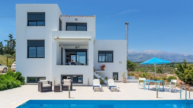 A modern two-story house with a swimming pool, outdoor seating, and a mountain view.