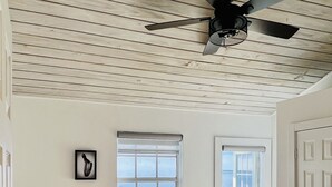 Un dormitori amb un llit, un ventilador de sostre, una finestra i una porta.