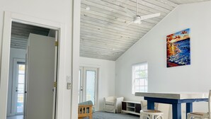Una habitació àmplia amb un sostre alt, un quadre a la paret, un escriptori amb dues cadires i una finestra que deixa entrar llum natural.