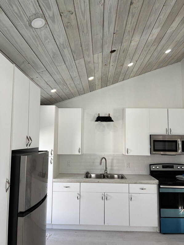 A modern kitchen with white cabinets, stainless steel appliances, and a wooden ceiling. - Waterfront Cottage in a Bimini oasis (Bimini)