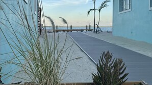 Un passeig marítim al costat de la platja, amb un pont de fusta, palmeres i vista a l'oceà.