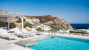 A poolside area with white lounge chairs and a clear view of a coastal town and the sea.