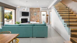 Ein modernes Wohnzimmer mit einem petrolfarbenen Sofa, einem Holzesstisch und einer Treppe mit beleuchteten Stufen.
