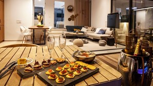 A modern dining area with a wooden table set for a meal, a sofa, and a glass partition. - Villa Ammos - Two Bedroom Villa, Sleeps 6 (Kavos)