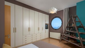 Une chambre avec une grande armoire, une fenêtre ronde, un lit et une échelle avec des étagères.