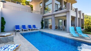 A modern two-story house with a swimming pool, blue lounge chairs, and a balcony. - Villa Arthur - Four Bedroom Villa, Sleeps 8 (Rhodes)