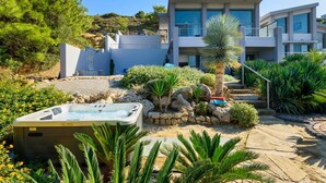 A modern two-story house with a hot tub in the garden, surrounded by tropical plants and a rocky landscape. - Villa Arthur - Four Bedroom Villa, Sleeps 8 (Rhodes)