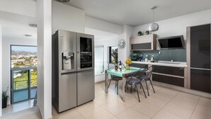 A modern kitchen with a large refrigerator, a dining table with chairs, and a view of the city through large windows. - Villa Arthur - Four Bedroom Villa, Sleeps 8 (Rhodes)