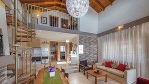 A spacious living area with a dining table, sofa, and staircase leading to an upper level. - Villa Lardos - Four Bedroom Villa, Sleeps 10 (Rhodes)