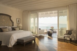 Un dormitorio amplio con una cama grande, un banco, una silla y vistas al océano a través de una puerta corrediza de vidrio.