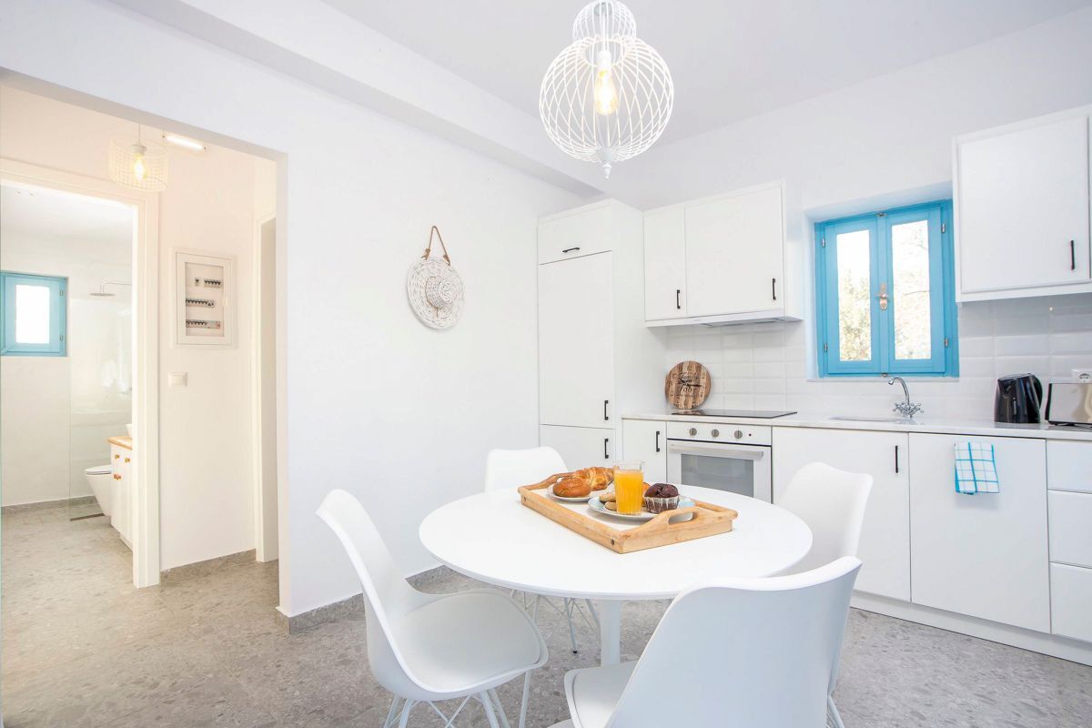 A modern kitchen with white cabinets, a round dining table, and a blue window.