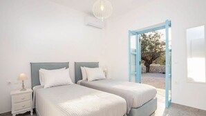 A bedroom with two beds, a nightstand, and a door leading to an outdoor area. - Kalathos Aspro - Two Bedroom Villa, Sleeps 4 (Kalathos)