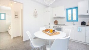 A modern kitchen with white cabinets, a round dining table, and a blue window. - Kalathos Aspro - Two Bedroom Villa, Sleeps 4 (Kalathos)