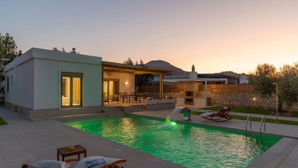 Une maison moderne dotée d’une piscine, d’un espace salon extérieur et d’un mur en pierre.