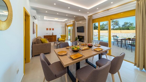 A modern dining area with a wooden table set for four, surrounded by chairs. - Kolympia Illios - Two Bedroom Villa, Sleeps 6 (Kolympia)