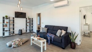 A modern living room with a dark sofa, white coffee table, and shelves with decorative items. - Kolympia Petra - Two Bedroom Villa, Sleeps 6 (Kolympia)