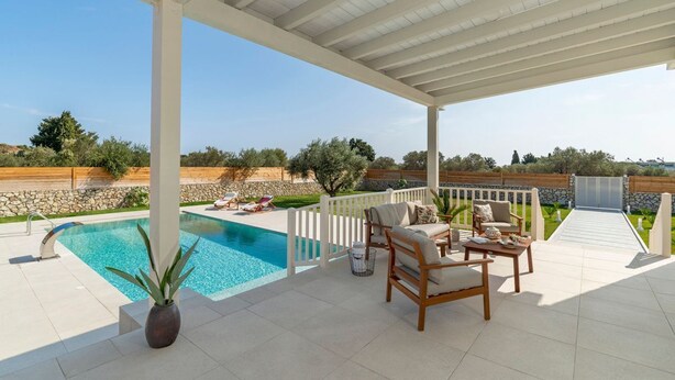 A covered outdoor area with a pool, lounge chairs, and a view of the surrounding landscape. - Kolympia Petra - Two Bedroom Villa, Sleeps 6 (Kolympia)