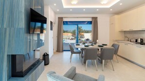 A modern living room with a flat-screen TV, a sofa, and a dining area with a table and chairs.