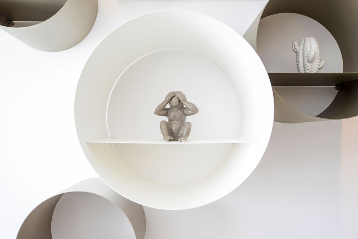 Un intérieur minimaliste avec une sculpture centrale posée sur une étagère blanche, entourée d’étagères circulaires décorées de cactus.