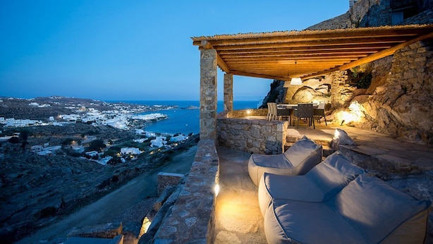 Un patio de piedra con una pérgola de madera, mobiliario exterior y vistas a la costa.